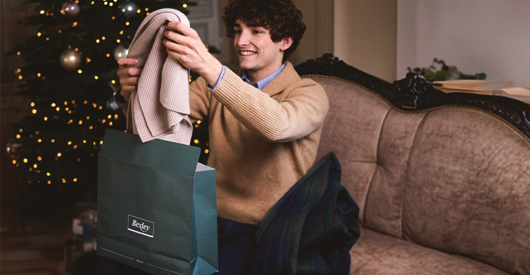 Jeune homme déballant un cadeau élégant près d'un sapin de Noël.