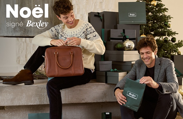 Jeune homme déballant un cadeau élégant près d'un sapin de Noël.